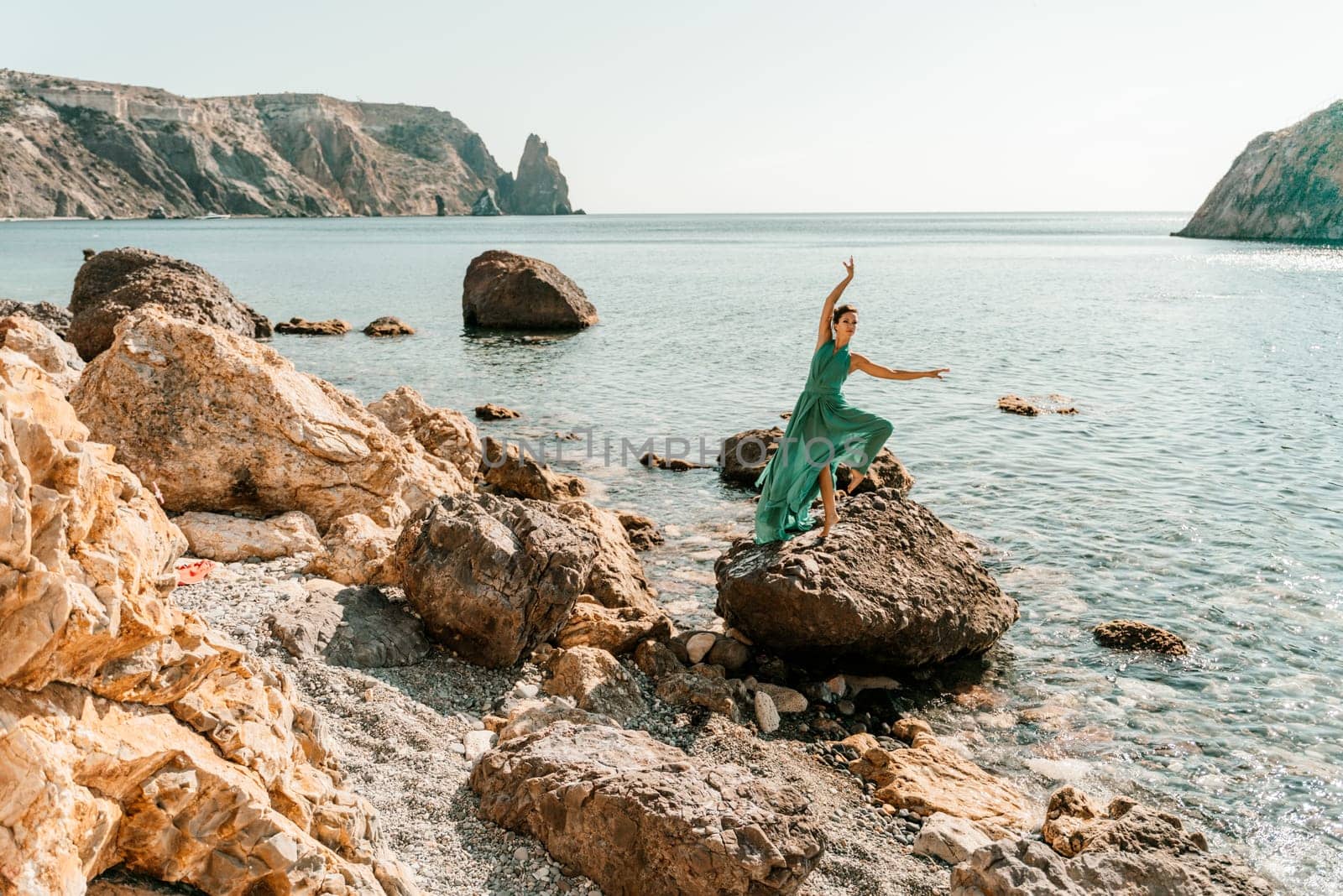 Woman green dress sea. Woman in a long mint dress posing on a beach with rocks on sunny day. Girl on the nature on blue sky background. by Matiunina