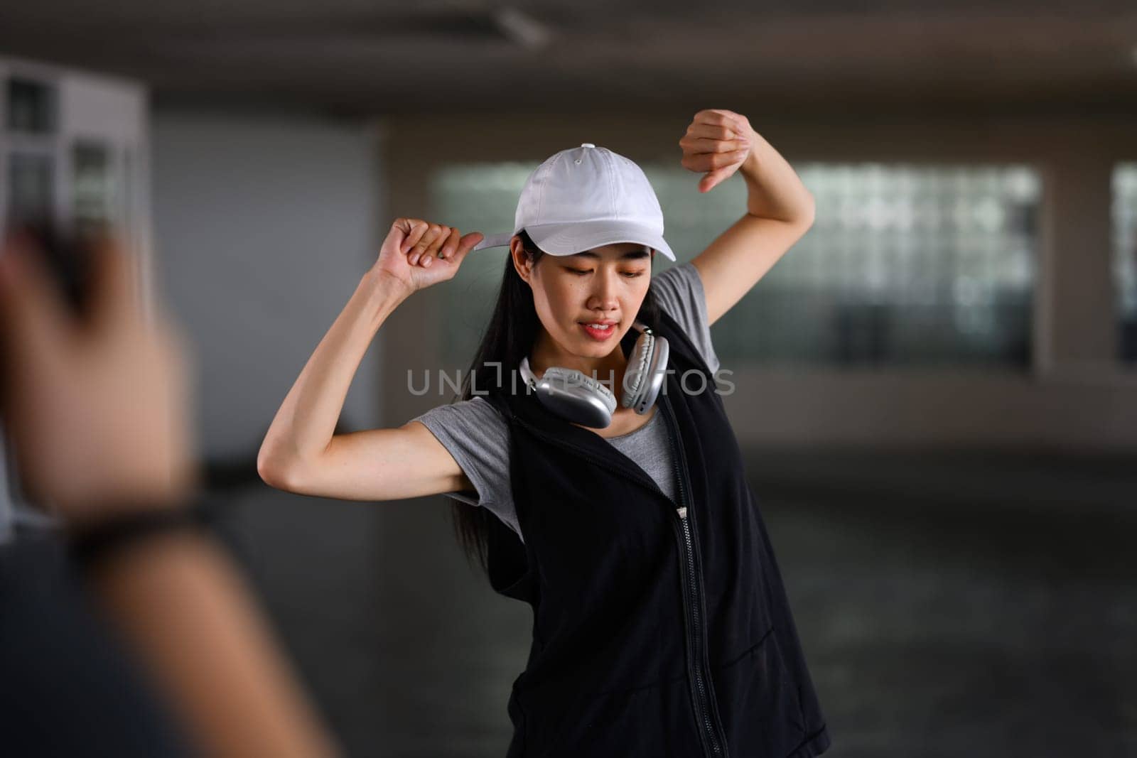 Woman dancing in style of hip hop in parking garage with videographer shooting video on digital camera by prathanchorruangsak
