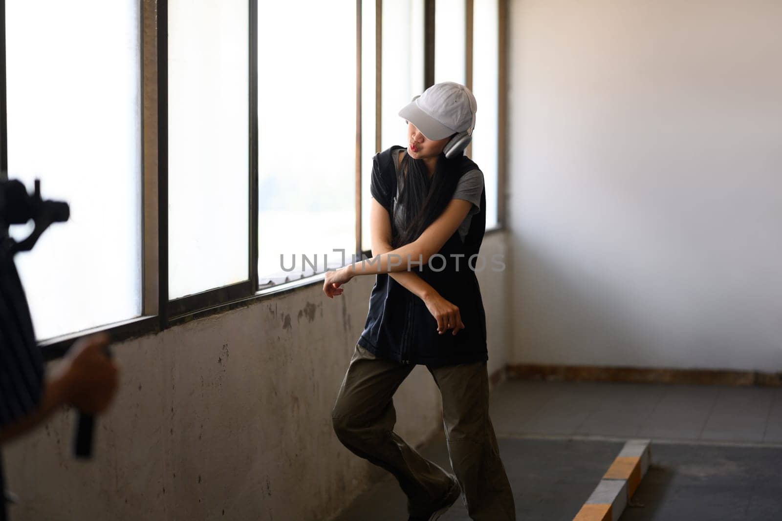 Young woman dancing in parking garage while man shooting with a professional camera by prathanchorruangsak