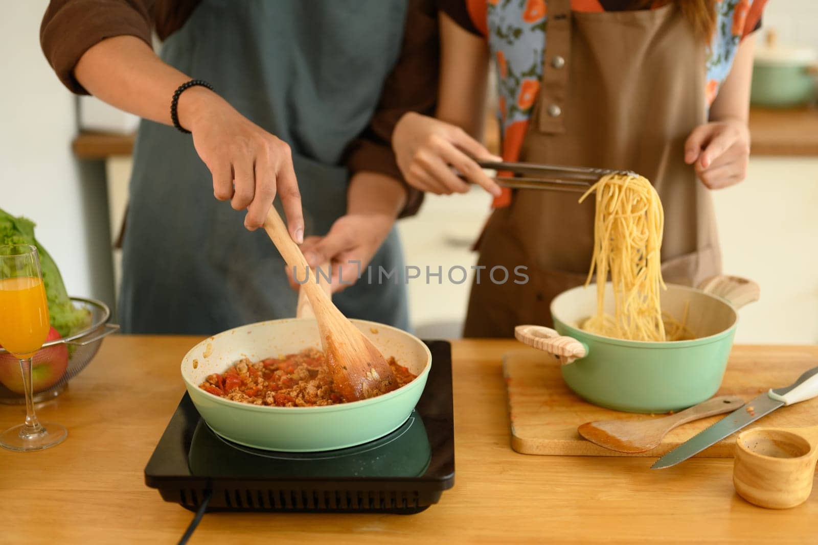Shot of happy young couple wearing aprons making delicious bolognese sauce for dinner in kitchen by prathanchorruangsak