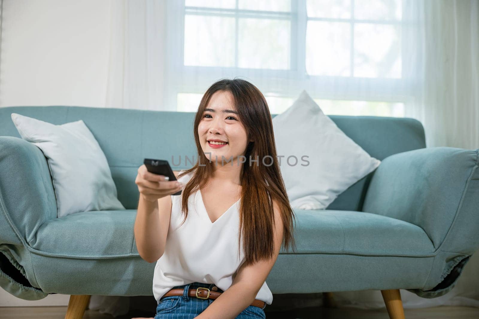 Happy female fun comedy video holding remote watching television, Asian young woman smiling sitting relaxing watch TV holding remote control on sofa in living room, Activity lifestyles concept