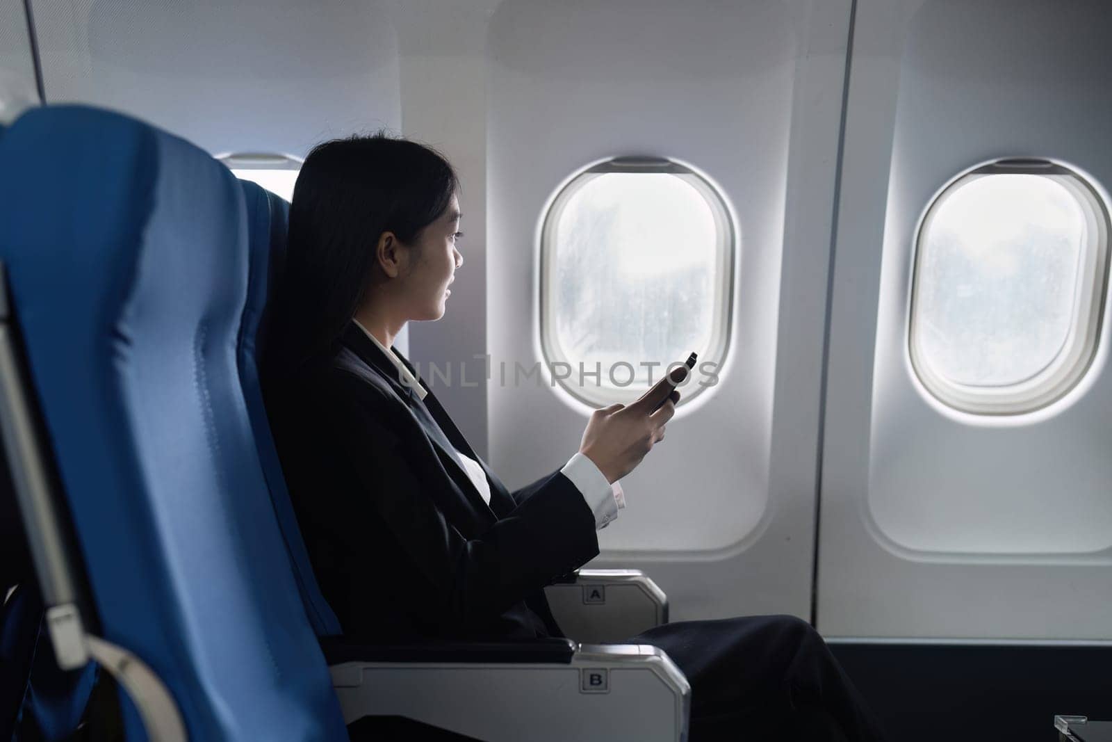 Beautiful Asian businesswoman using mobile phone in aeroplane. working, travel, business concept by itchaznong