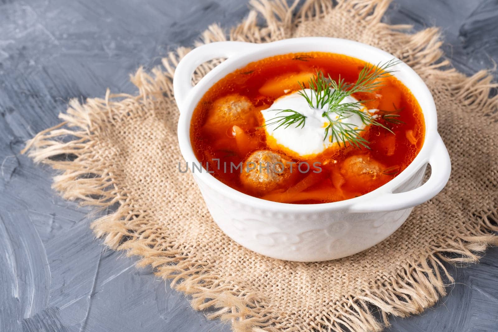 Close up borscht with sour cream in a bowl with bread on a gray table.