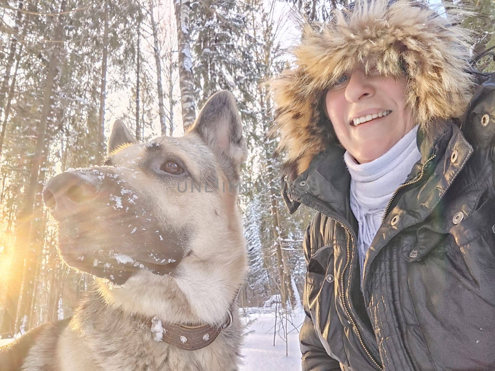 Adult girl with shepherd dog taking selfies in winter forest. Middle aged woman and big shepherd dog on nature in cold day. Friendship, love, communication, fun, hugs