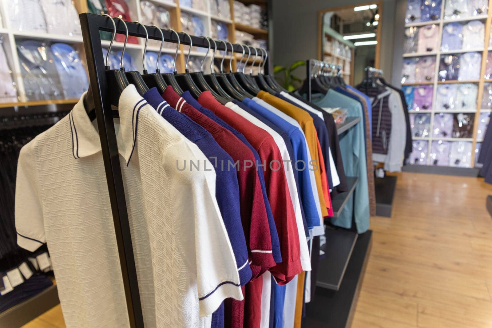 Closed up multicolored mens polo shirts on hangers and shelves in a men's clothing store.