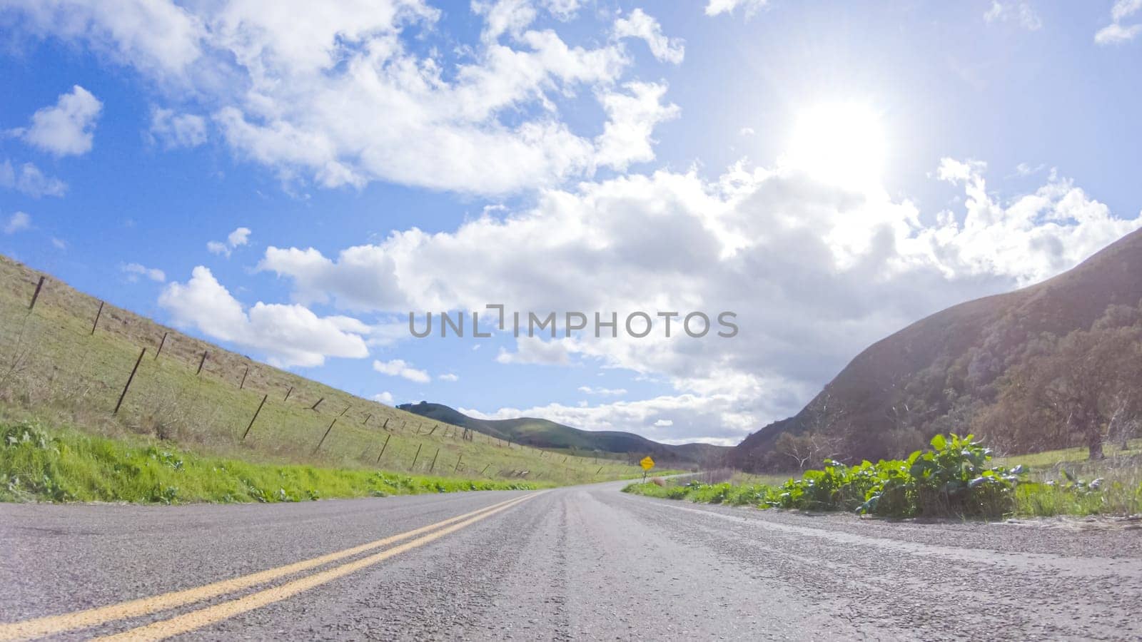 Vehicle is cruising along the Cuyama Highway under the bright sun. The surrounding landscape is illuminated by the radiant sunshine, creating a picturesque and inviting scene as the car travels through this captivating area.