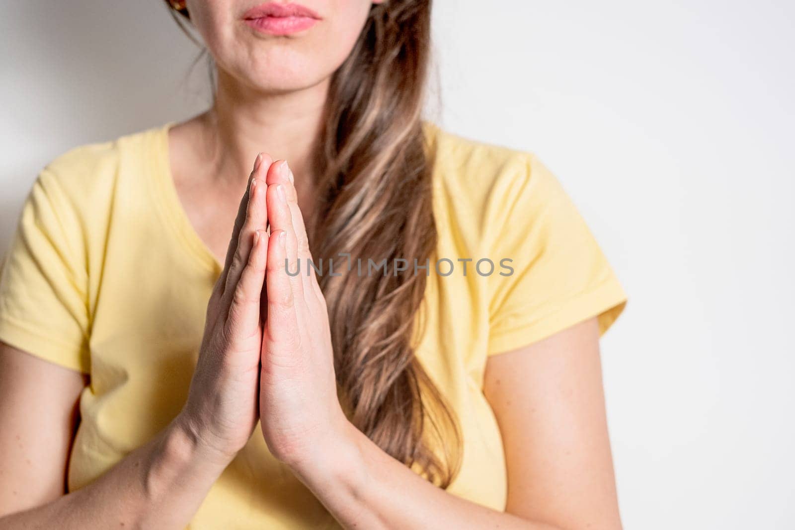 Closeup portrait of a young woman praying on light background.