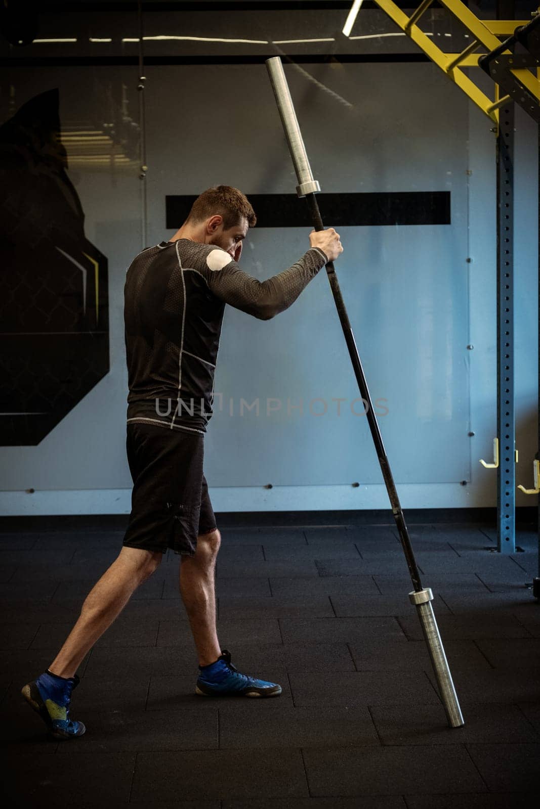 Concentrated young adult male boxer practicing barbell exercise designed to mimic boxing movements, targeting muscle groups used in punches for explosive strength during workout at gym