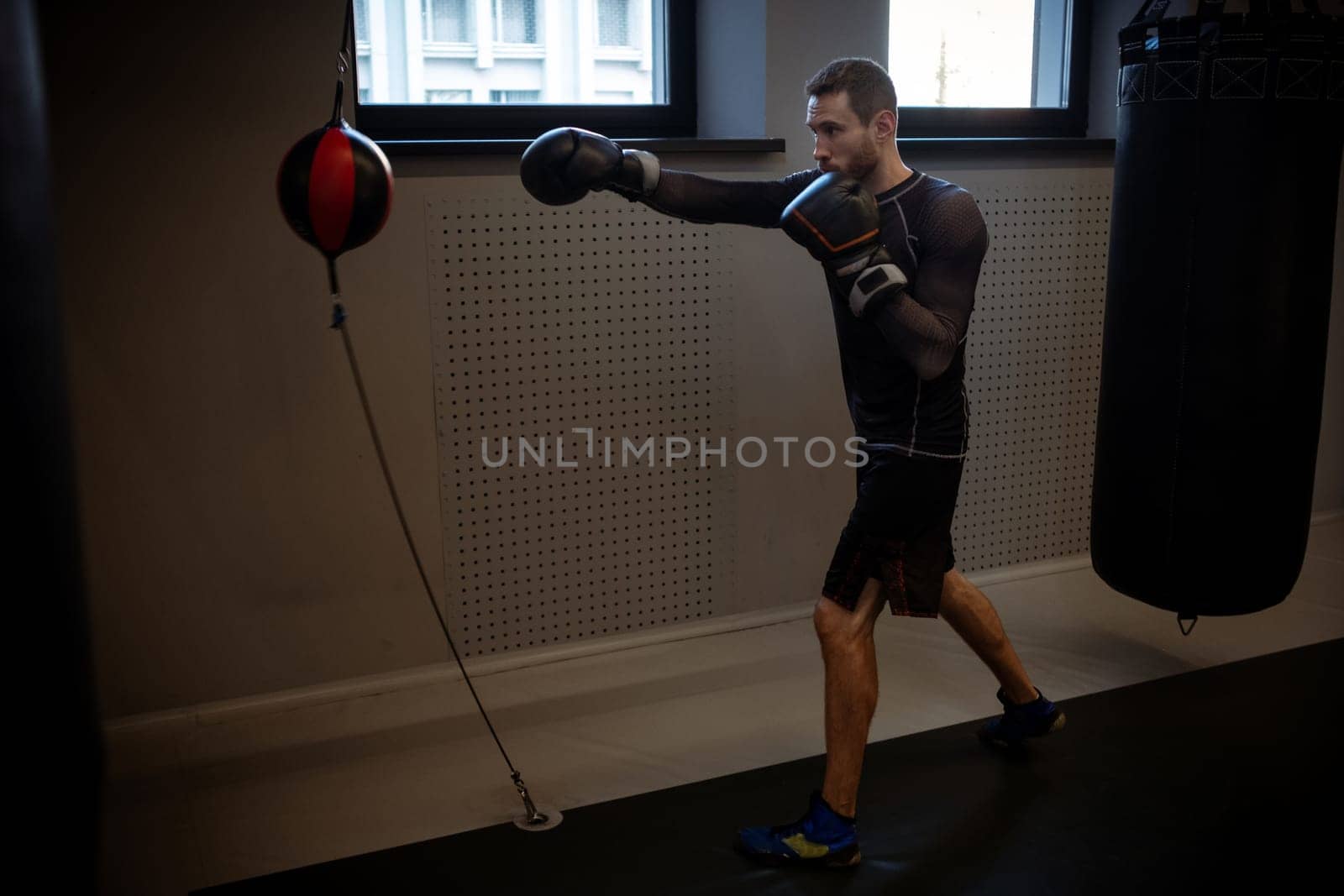 Young adult boxer focused on improving punch speed and accuracy with floor to ceiling bag while training alone in modern boxing gym. Sports motivation concept
