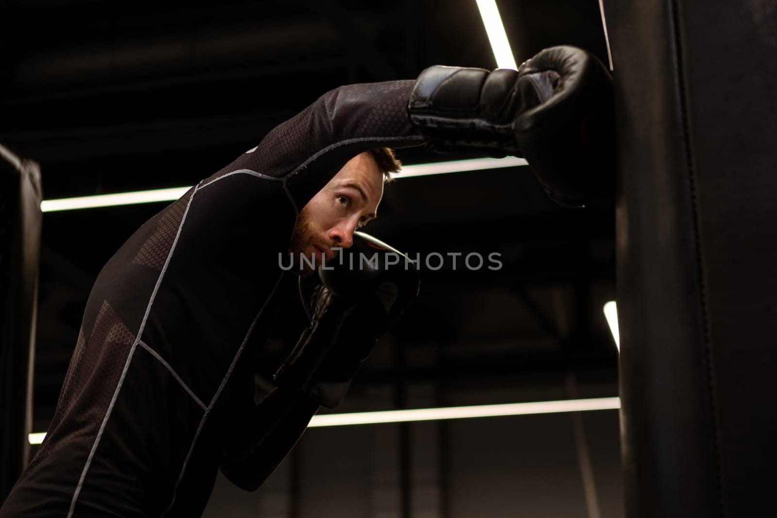 Concentrated boxer practicing punches on heavy bag in gym by nazarovsergey