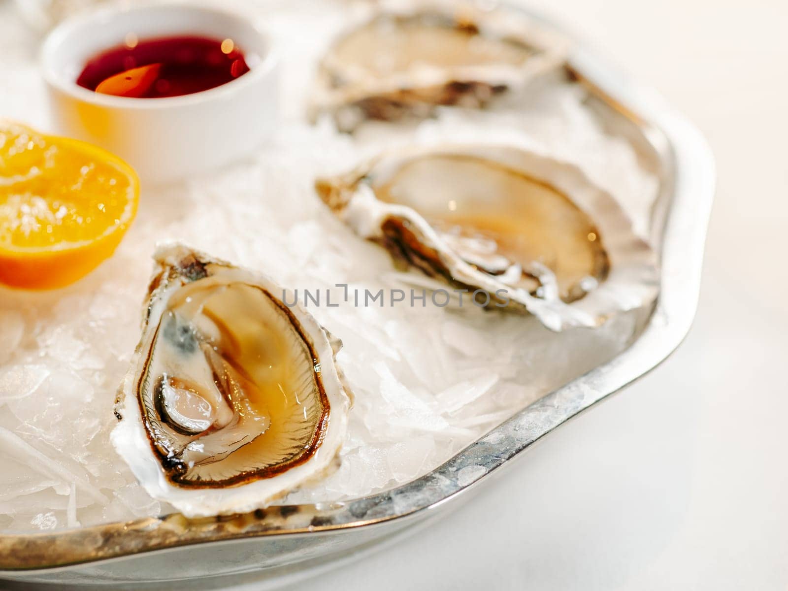 Woman having oysters at table. Fresh oysters on large plate with ice and lemon. Healthy food, gourmet food, restaurant food. Mediterranean cuisine, girl eats, oysters on ice