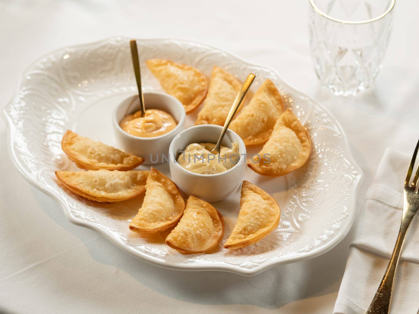 Hot Appetizers with Mini Chebureki and sauces Isolated on white table background. Restaurant Starter Menu with Crispy Burnt Turnovers, Pies or Samosa with Spicy Sause Close Up