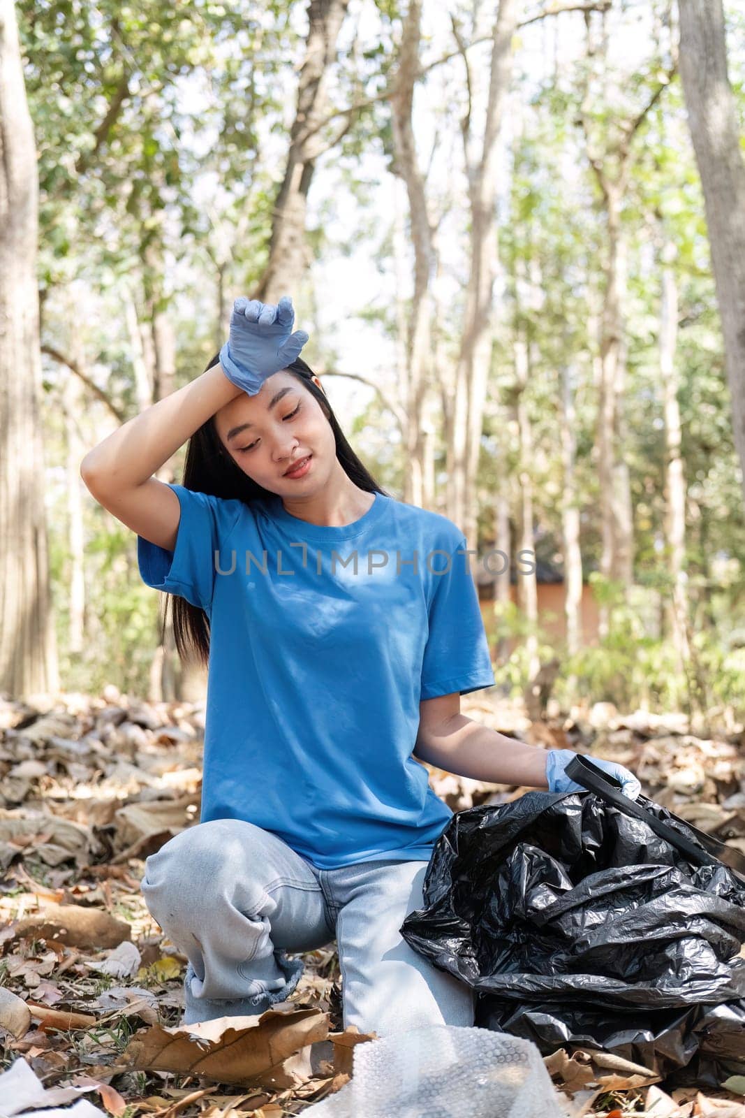 woman holds a garbage bag and a group of Asian volunteers clean up the area in the forest to preserve the natural ecosystem.