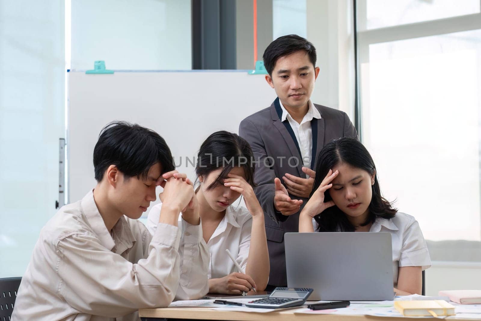A team of Asian businessmen discusses managing stressful office work in an office conference room..