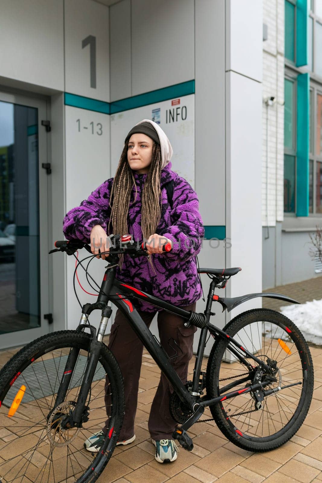 Bicycle rental concept. A young woman with dreadlocks in a purple fur coat rides a bicycle.