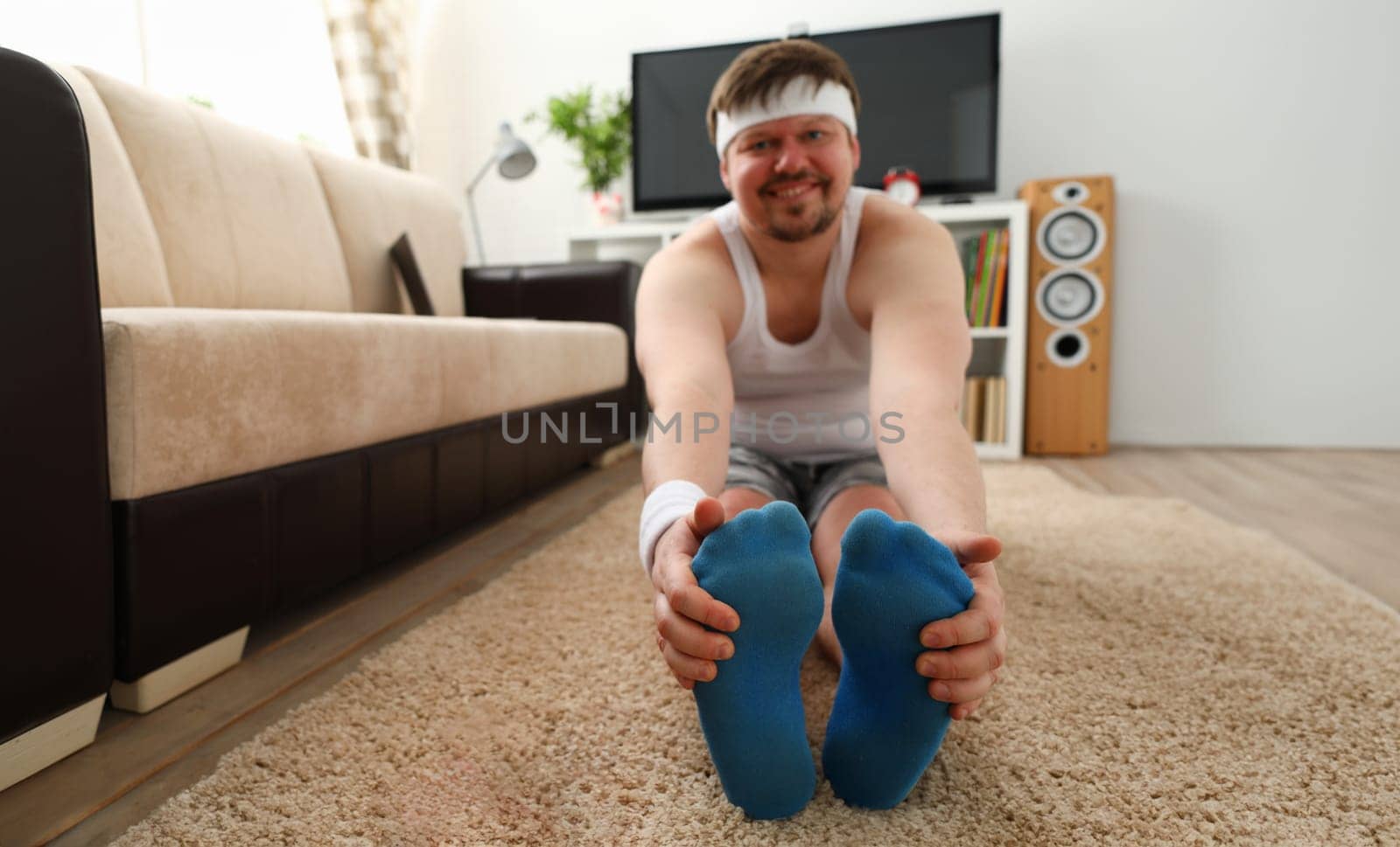 Young attractive fitness man lies on a fat mat with overweight performs stretching exercises and smiles