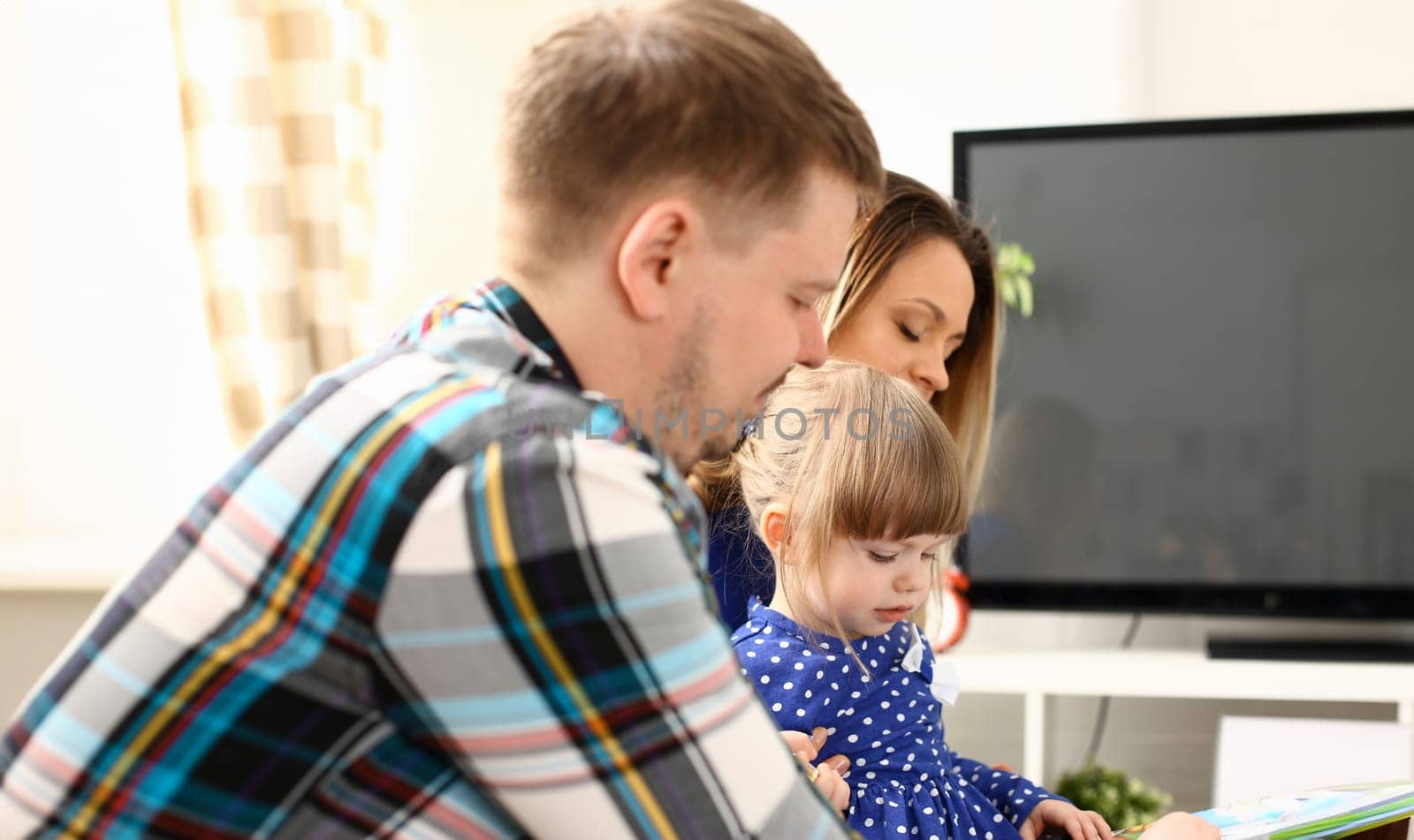 Happy parents with daughter at sofa at home. Beautiful smiling woman and handsome man play with cute little girl childhood and parenthood concept