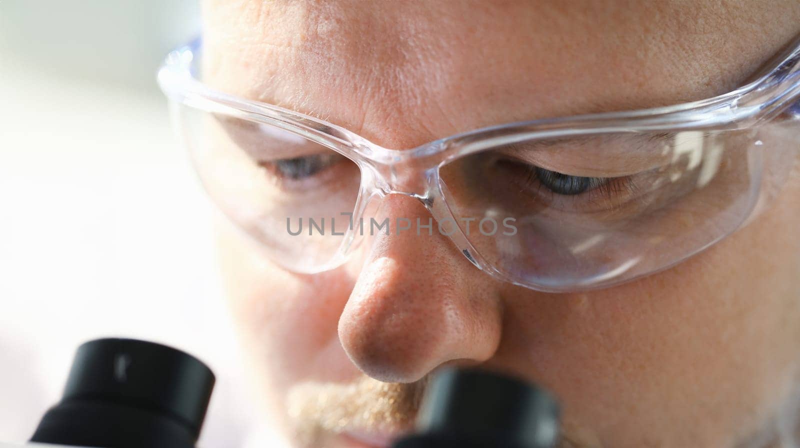 Handsome man scientist looking through binocular microscope examining diseases of the virus that infects water vivo ivf