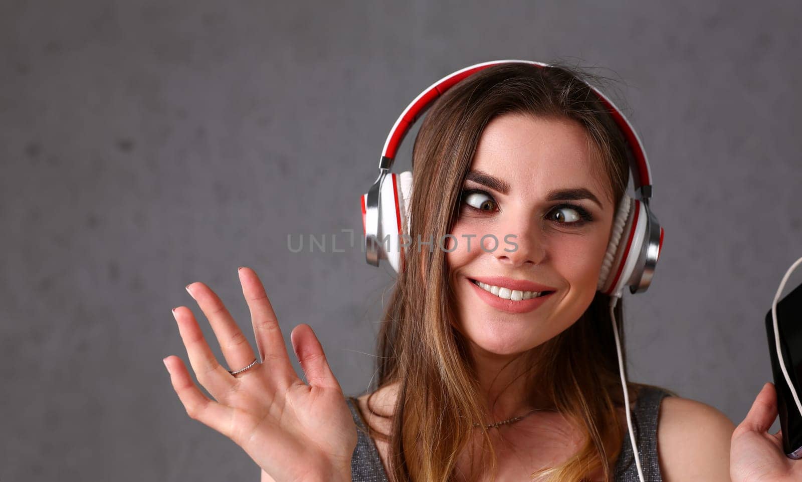 Beautiful blonde smiling woman with eyes closed wearing headphones listening favourite music on grey background. Modern urban life audio book radio having moments with dance move concept