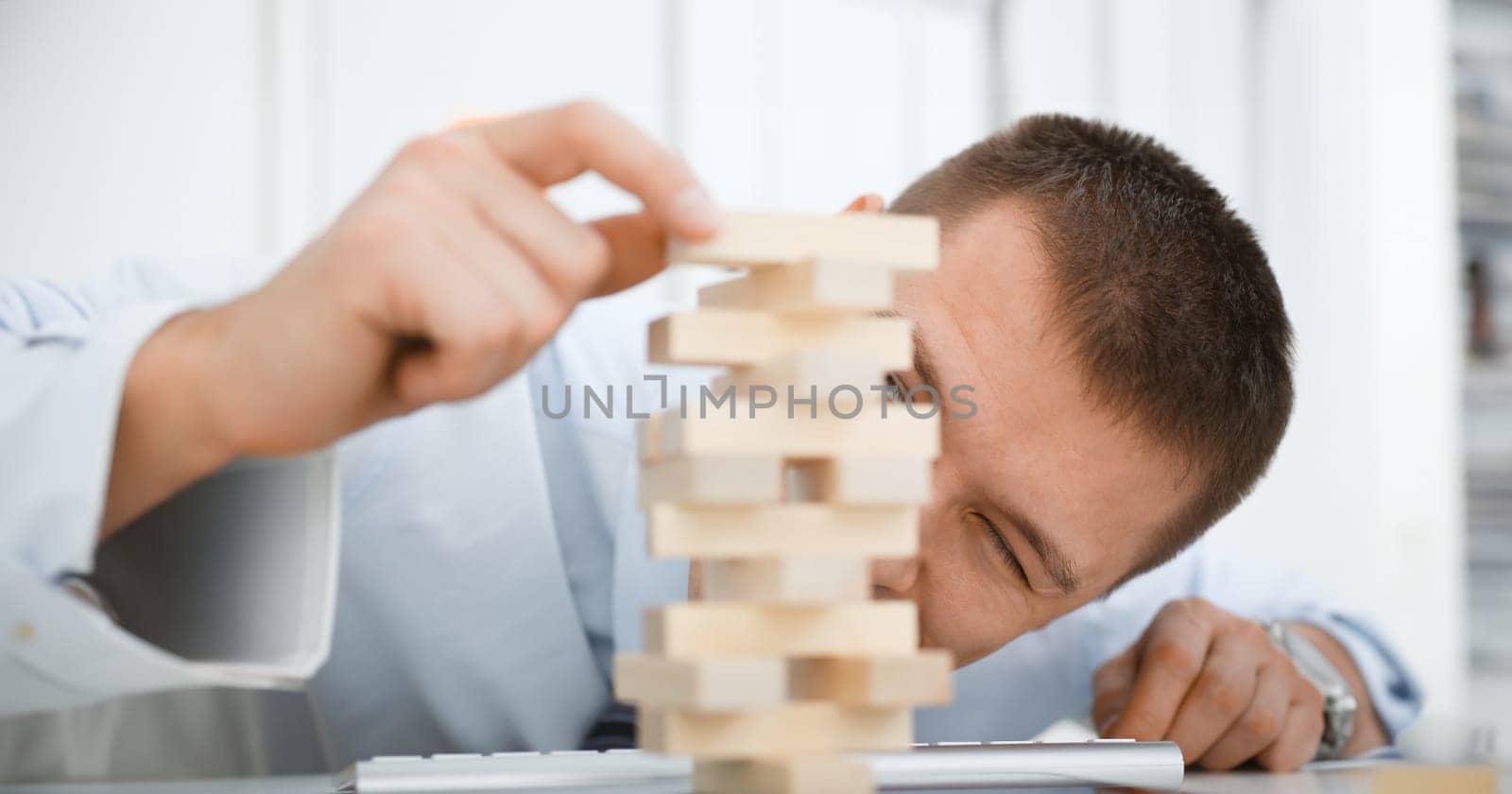 Businessman plays in strategy hand rearranging wooden blocks involved during break at work in office sitting table gaming pile fun joy pastime concept