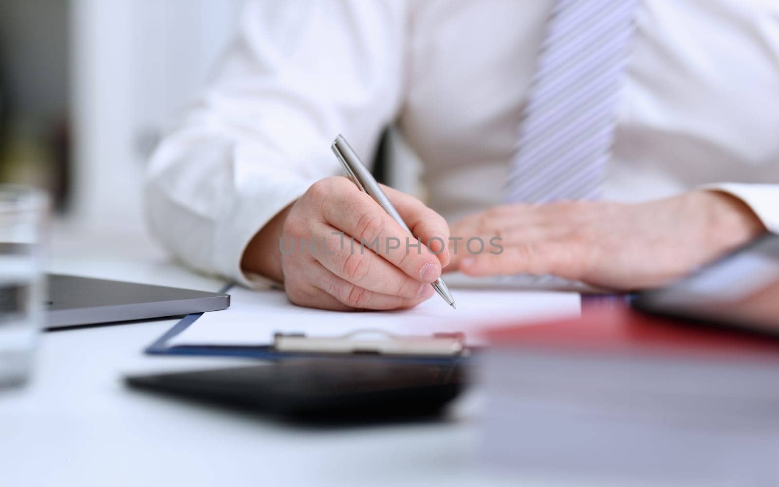 Male arm in suit and tie hold silver pen filling schedule in notepad at office workplace closeup. Legal law consult assistance gesture or finance investment advisor clerk job information gesture