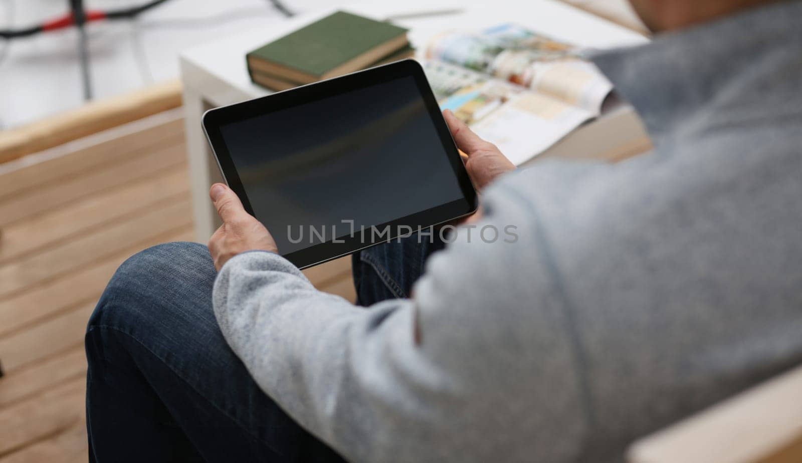 Male hand holds tablet pad in home setting while sitting on the couch engaged an internet surfing using application to press a finger on the display leisure listering music concept closeup.