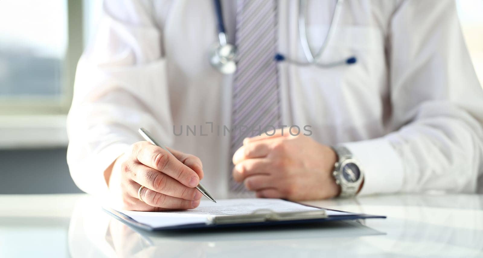 Male doctor hand hold silver pen filling patient history list at clipboard pad. Physical exam er disease prevention ward round visit check 911 prescribe remedy healthy lifestyle concept