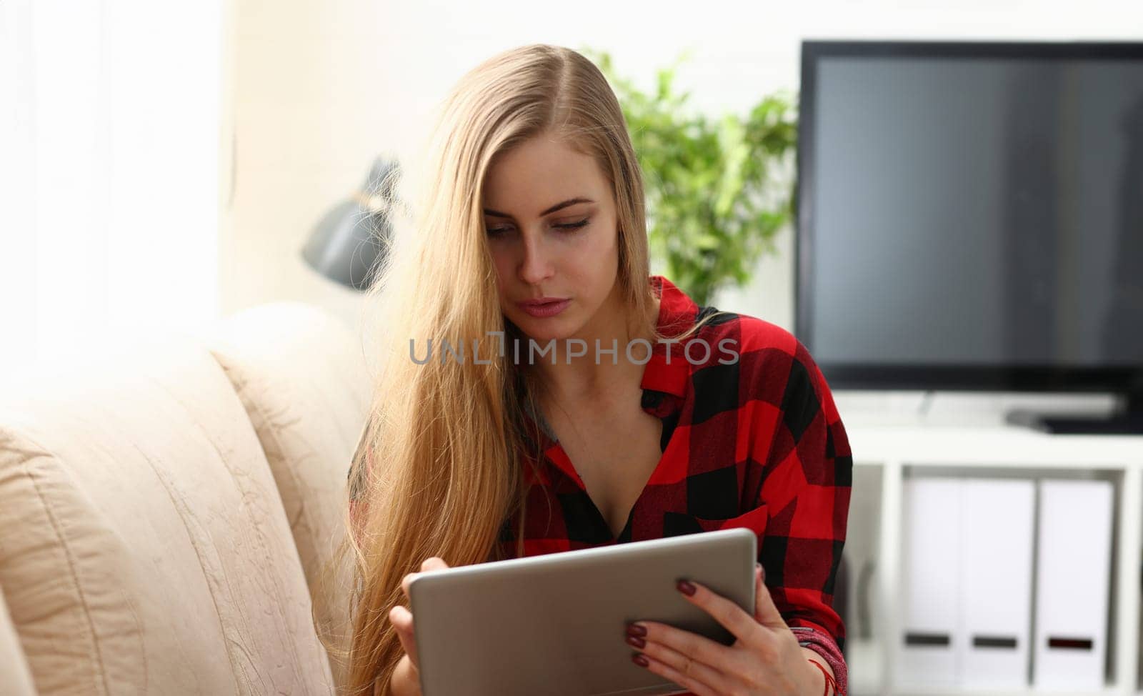 pretty blond young woman surfing the internet hold tablet in arms search information sit on sofa