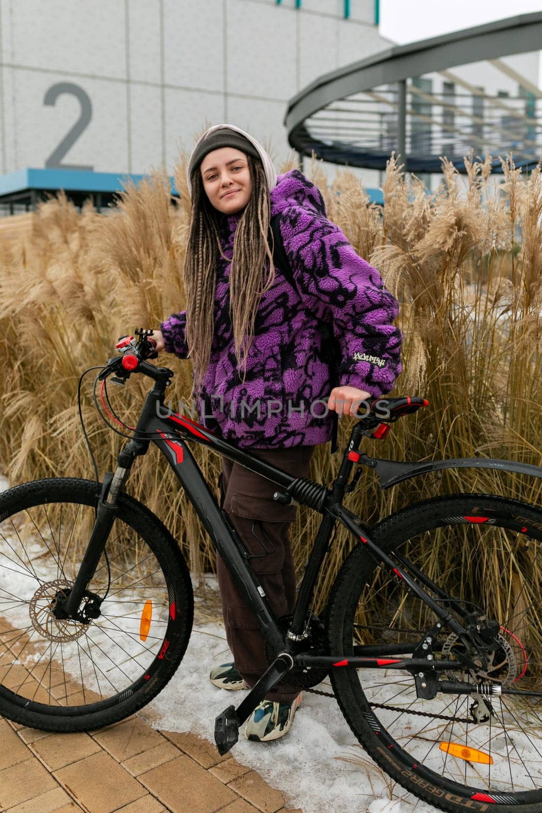 Lifestyle concept. Young woman with informal dreadlocks hairstyle rented a bicycle by TRMK