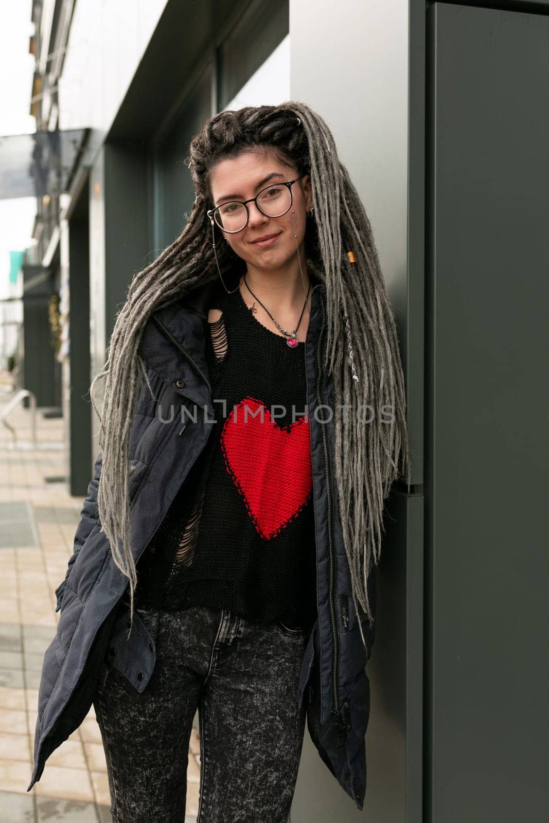 Photo on the street, young pretty informal woman with dreadlocks hairstyle smiling sweetly.