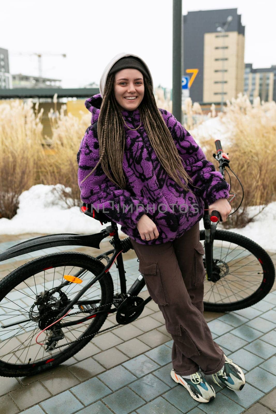 Cute young woman with piercing and dreadlocks rides a bicycle in winter.
