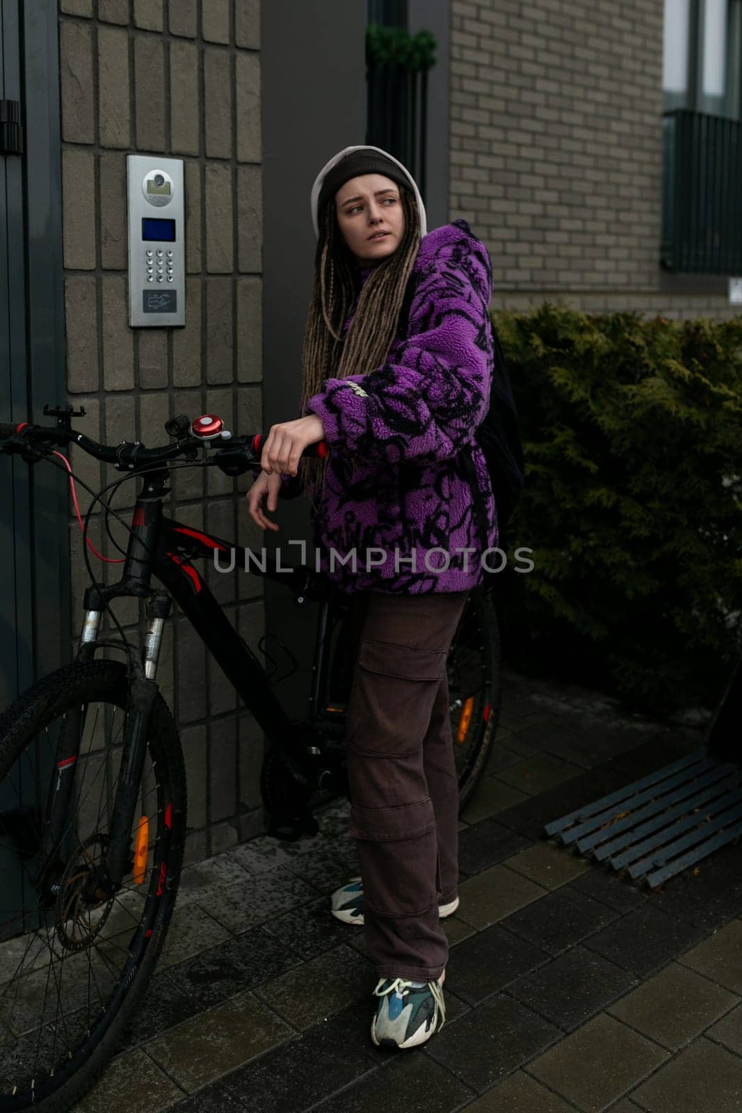 Nice young woman standing near the house with a bicycle.