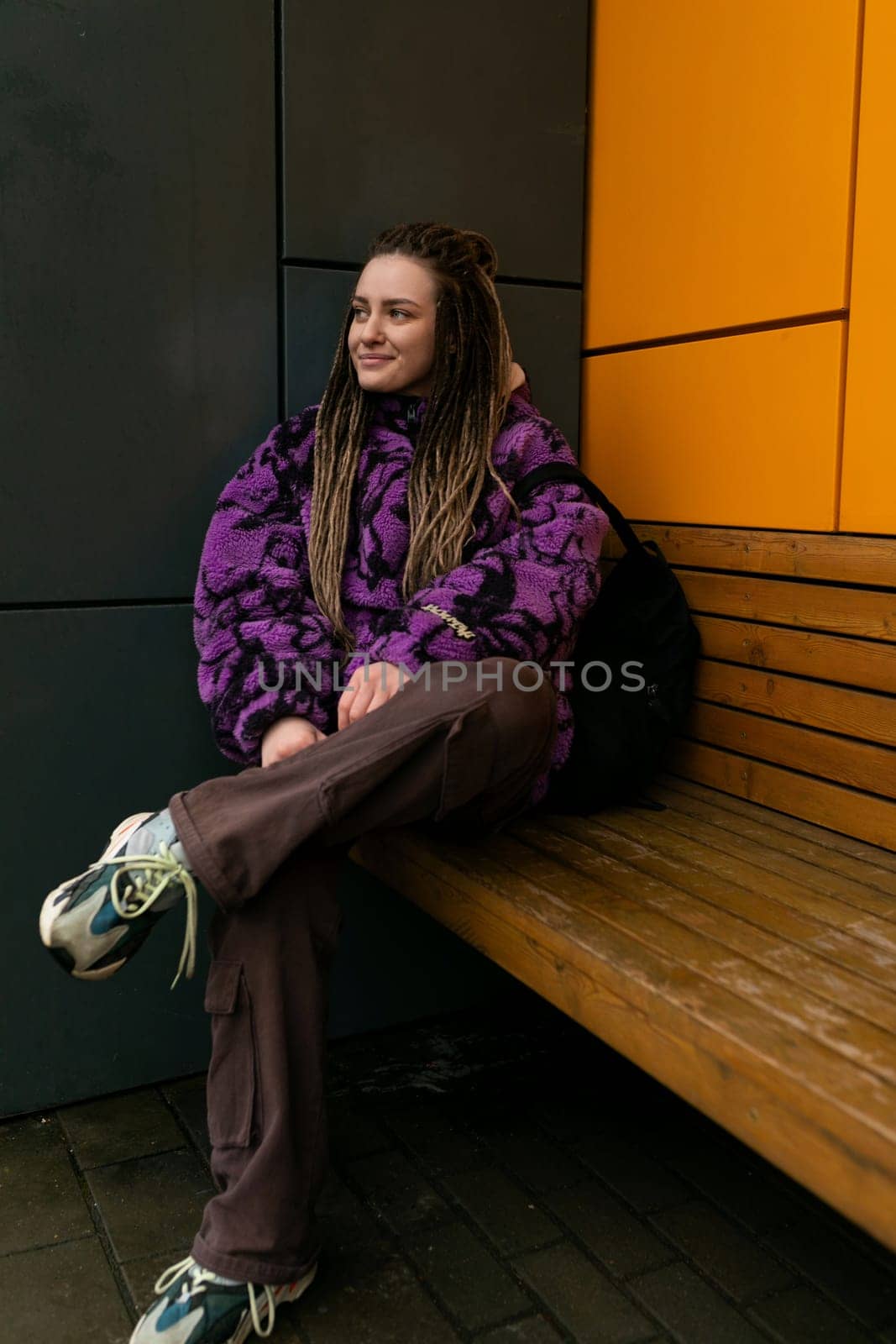 Lifestyle concept. A young woman with dreadlocks and piercings stands at the entrance to an orange house.