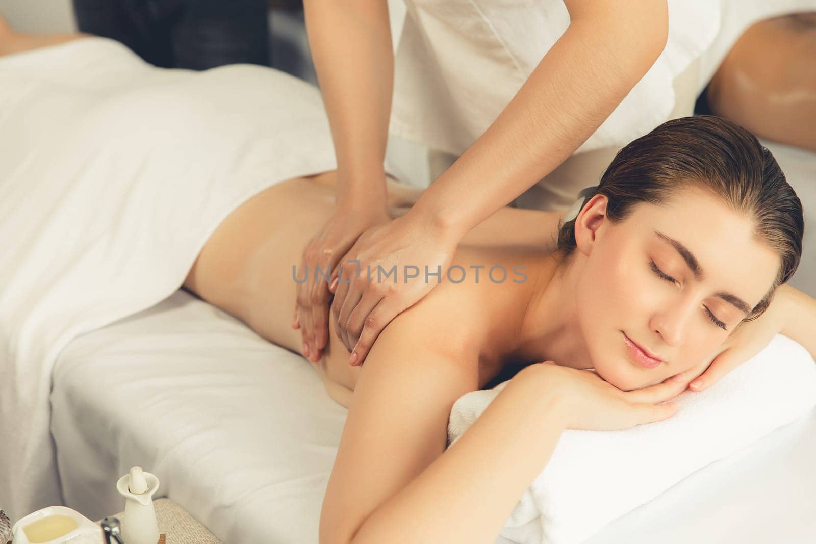 Caucasian couple customer enjoying relaxing anti-stress spa massage and pampering with beauty skin recreation leisure in day light ambient salon spa at luxury resort or hotel. Quiescent