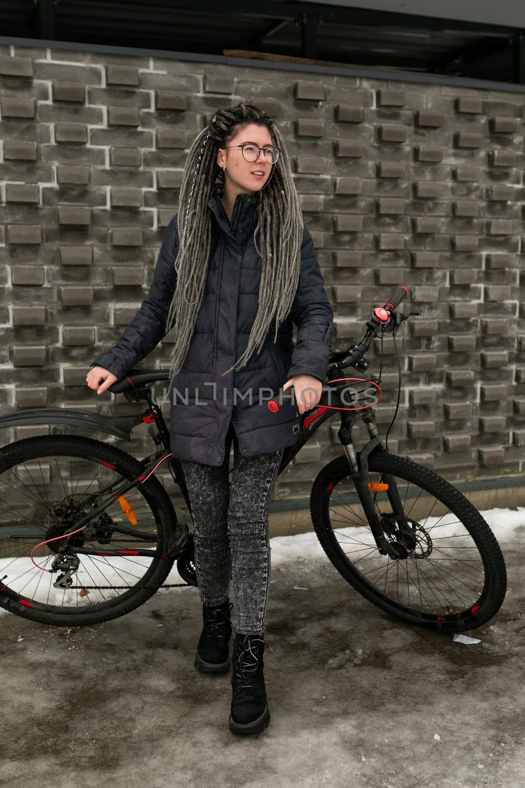 Cute young woman with dreadlocks hairstyle dressed in a winter jacket rides a bicycle by TRMK