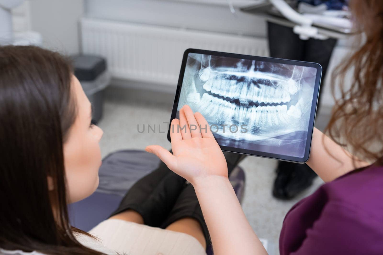 Utilizing a tablet to showcase the X ray image, the female dentist discusses treatment strategies with the patien