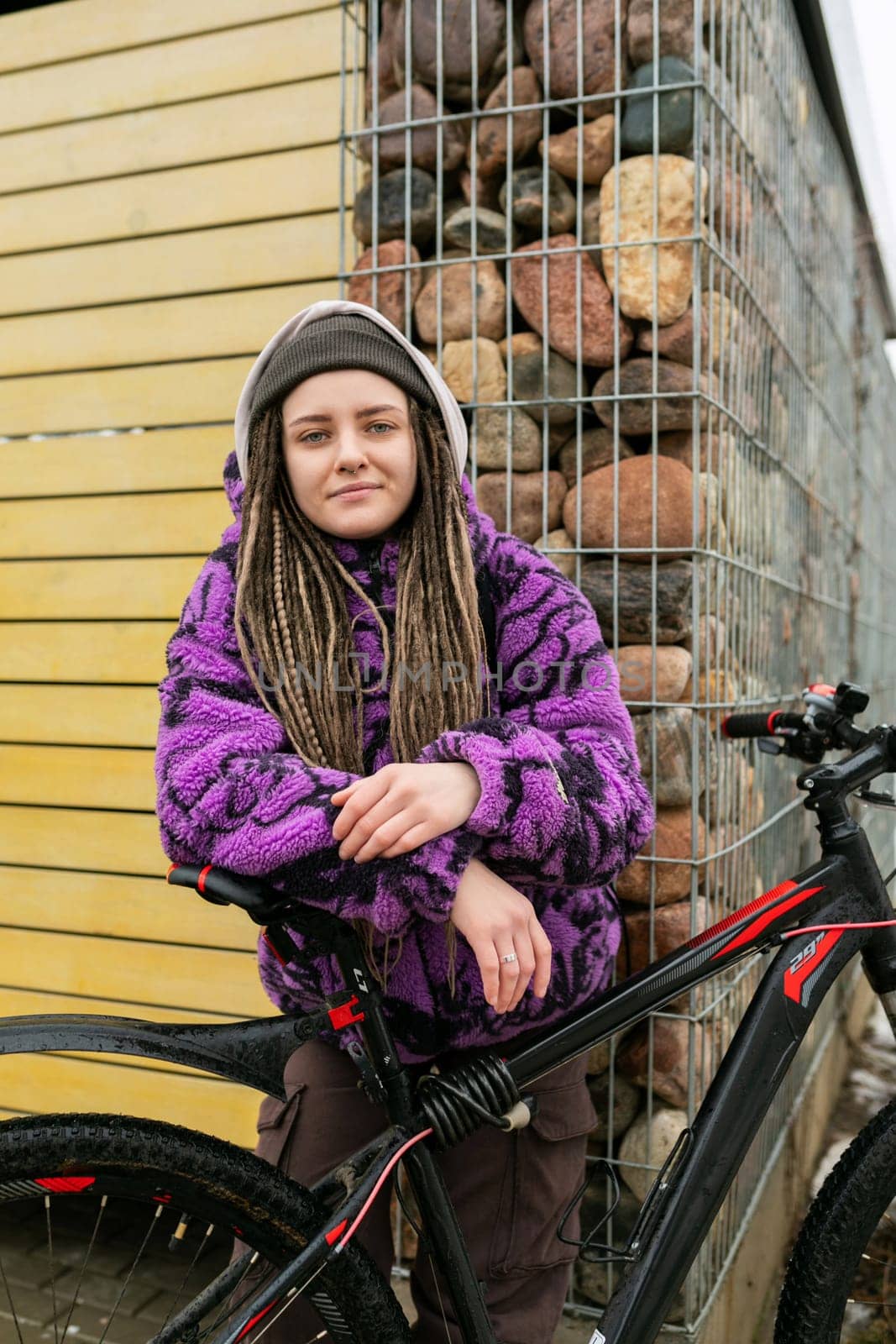 European stylish woman in an informal look with dreadlocks and piercings moves around the city on a bicycle.