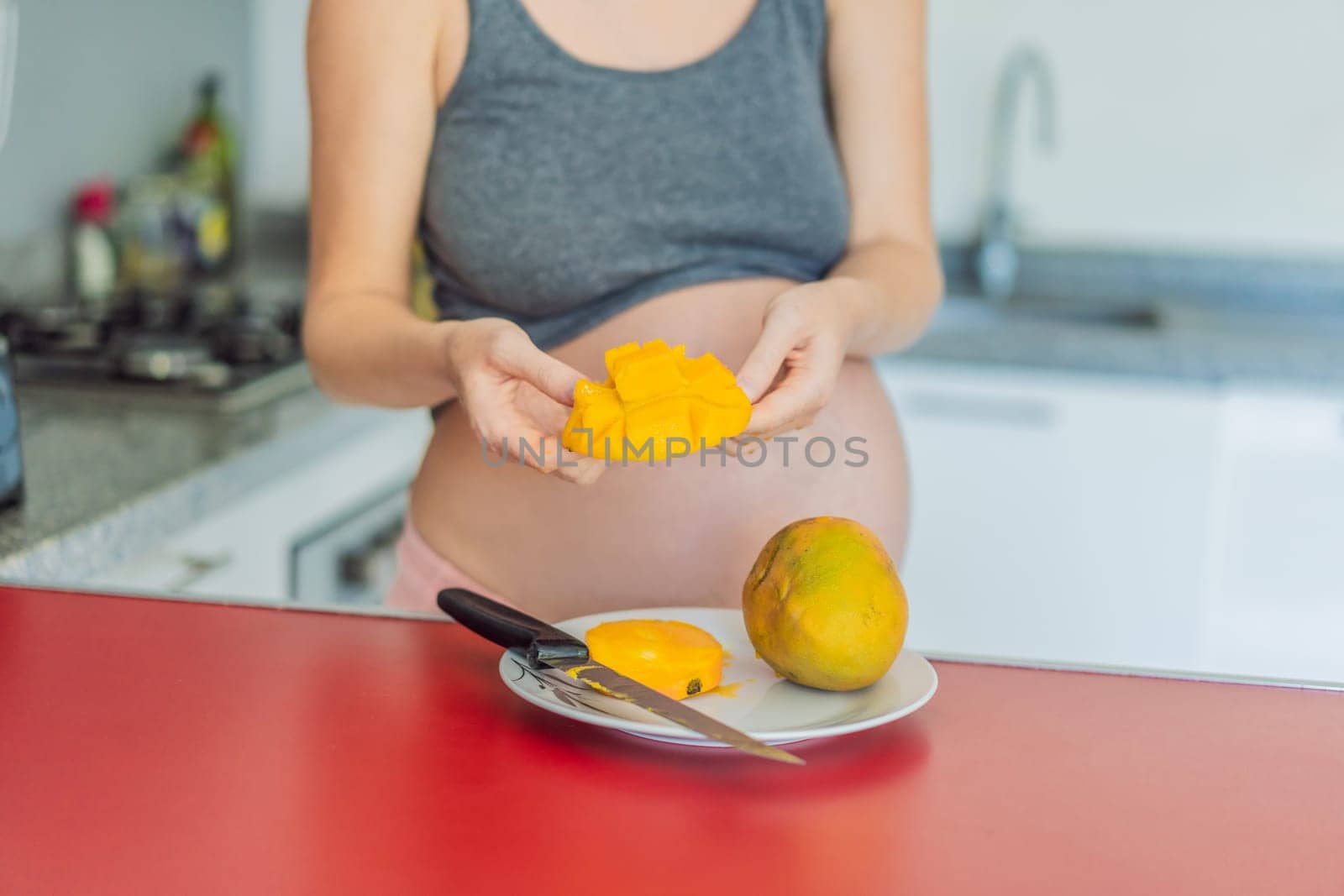 A skillful pregnant woman delicately cuts into a ripe mango, savoring a moment of culinary joy and nourishing her pregnancy with a fresh and flavorful treat by galitskaya