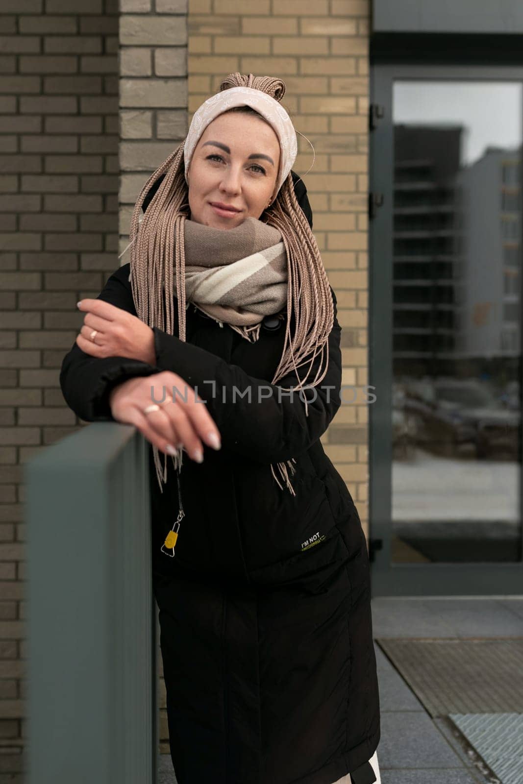Well-groomed young woman dressed in a winter black coat with a scarf in an urban environment.