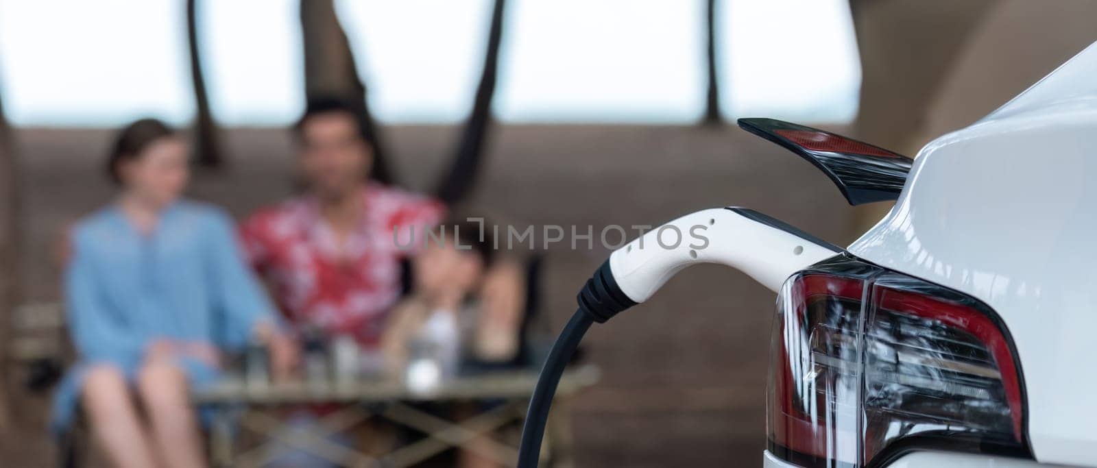 EV car charging with blurred family enjoying the seascape background. Perpetual by biancoblue