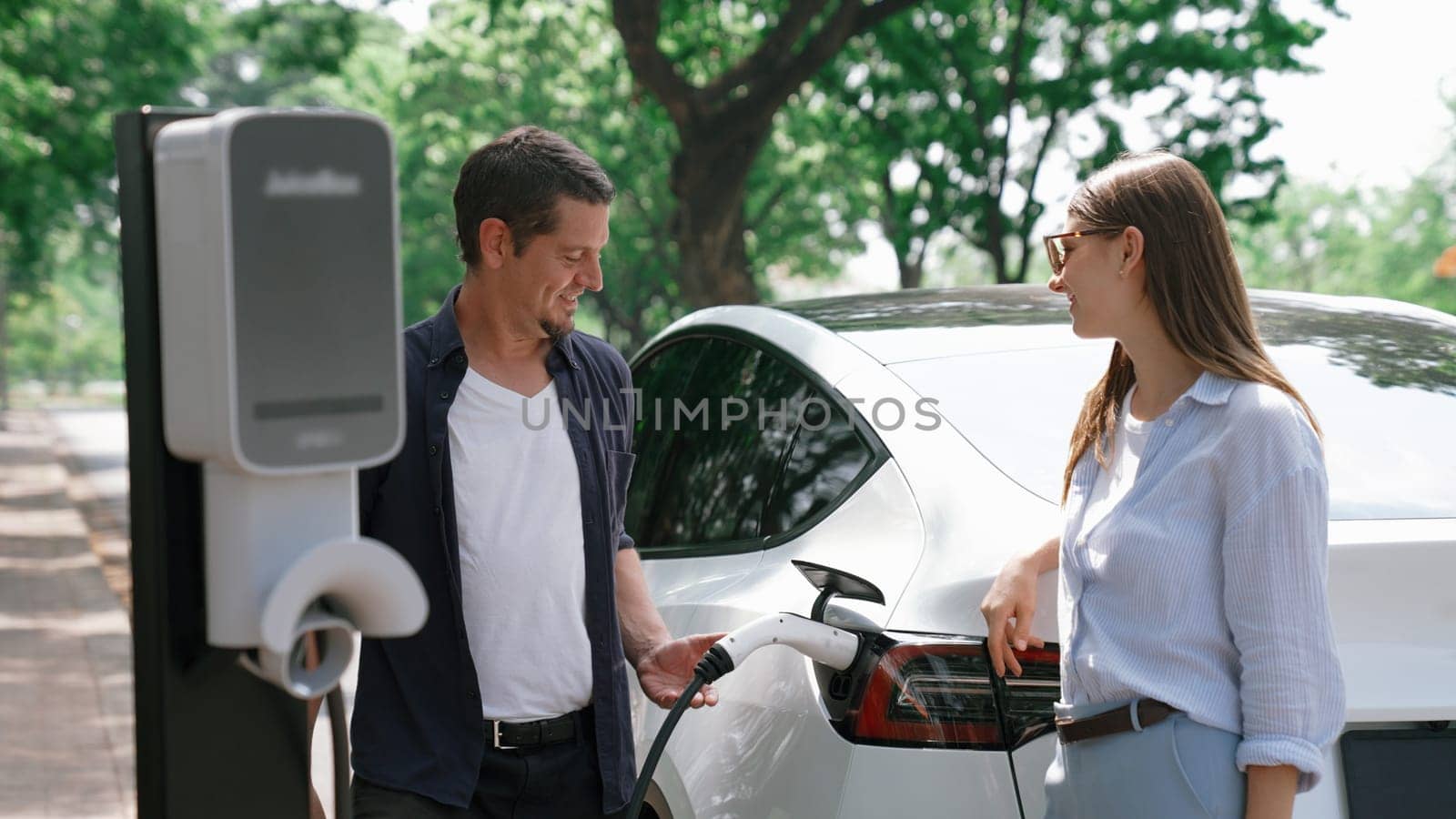 EV car recharging electricity for battery by lovey couple traveling during their road trip travel by eco friendly electric vehicle in national park and greenery forest on holiday. Exalt