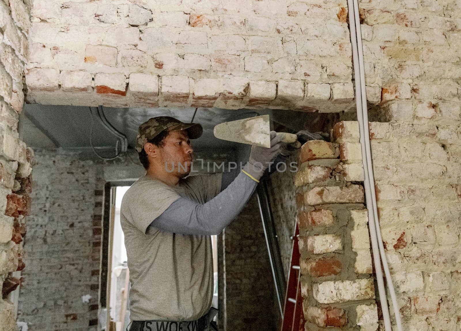 A young man places bricks in a doorway. by Nataliya