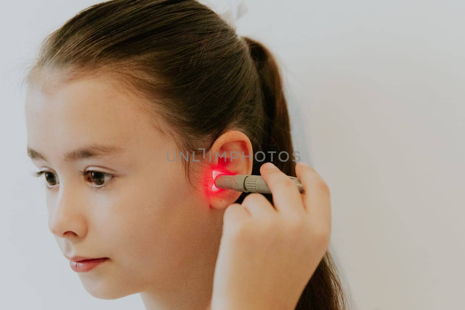 A girl treats her ear with an infrared light device. by Nataliya