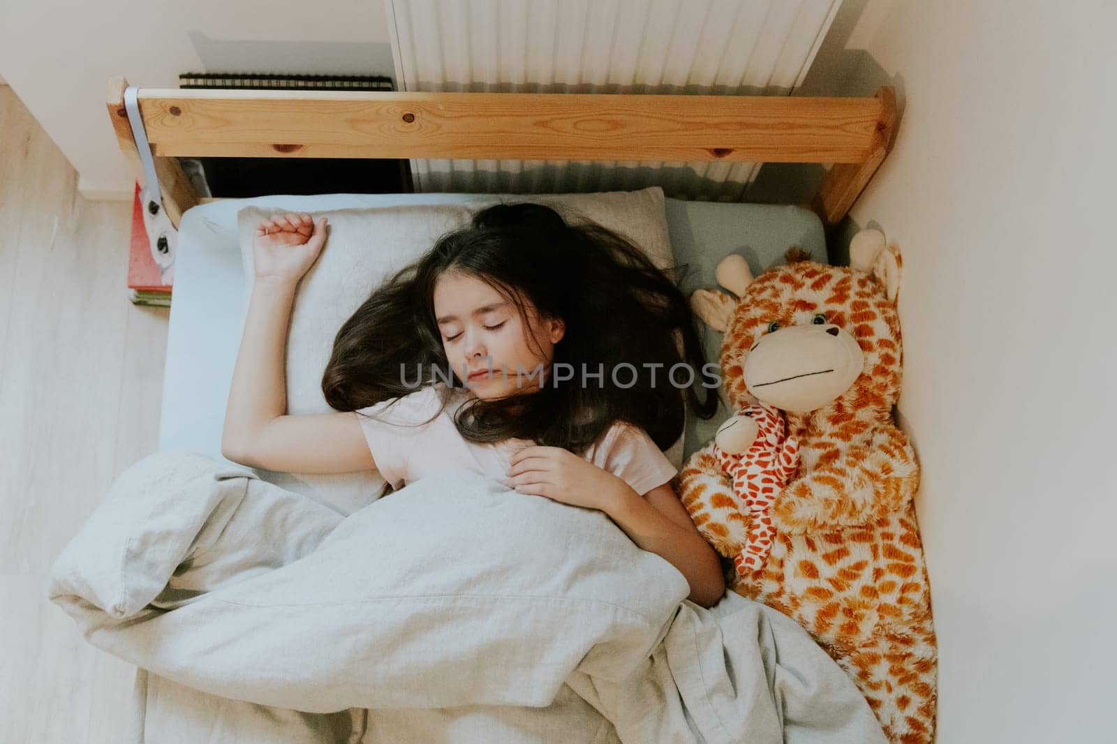 A little girl sleeps in bed with a giraffe toy. by Nataliya