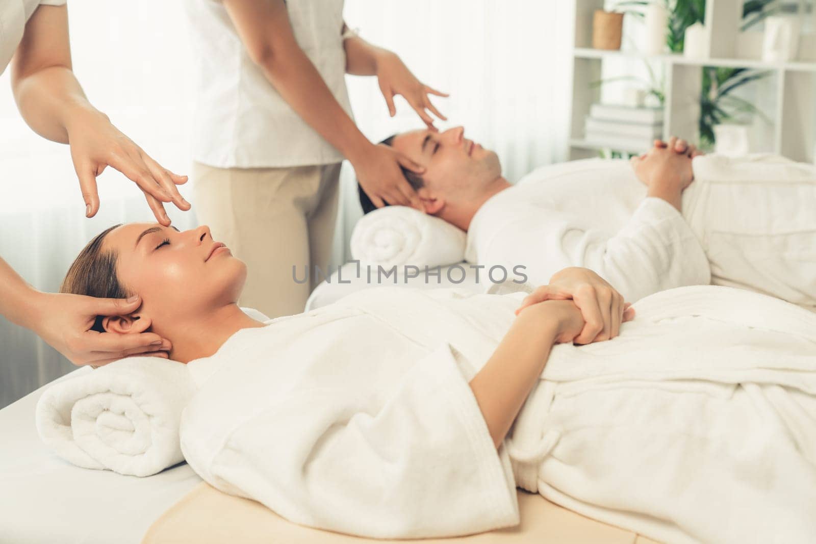 Caucasian couple enjoying relaxing anti-stress head massage and pampering facial beauty skin recreation leisure in dayspa modern light ambient at luxury resort or hotel spa salon. Quiescent