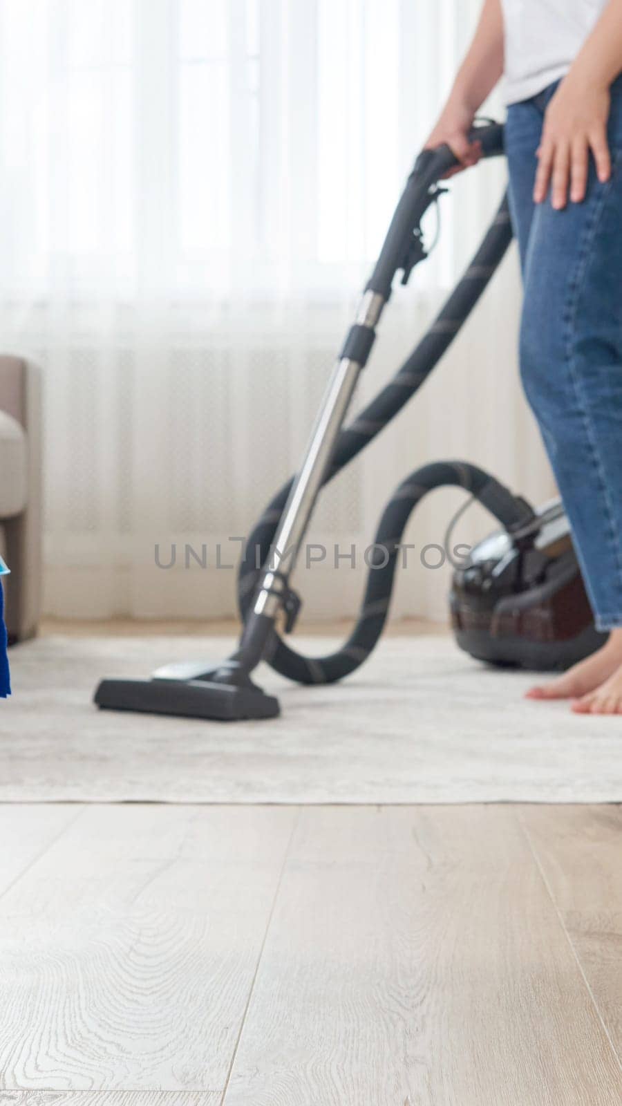 Woman cleaning the carpet with vacuum cleaner in the living room by Mariakray