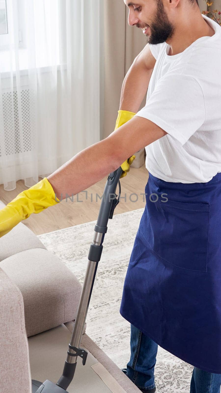 Young man Cleaning sofa With Vacuum Cleaner in leaving room At Home by Mariakray