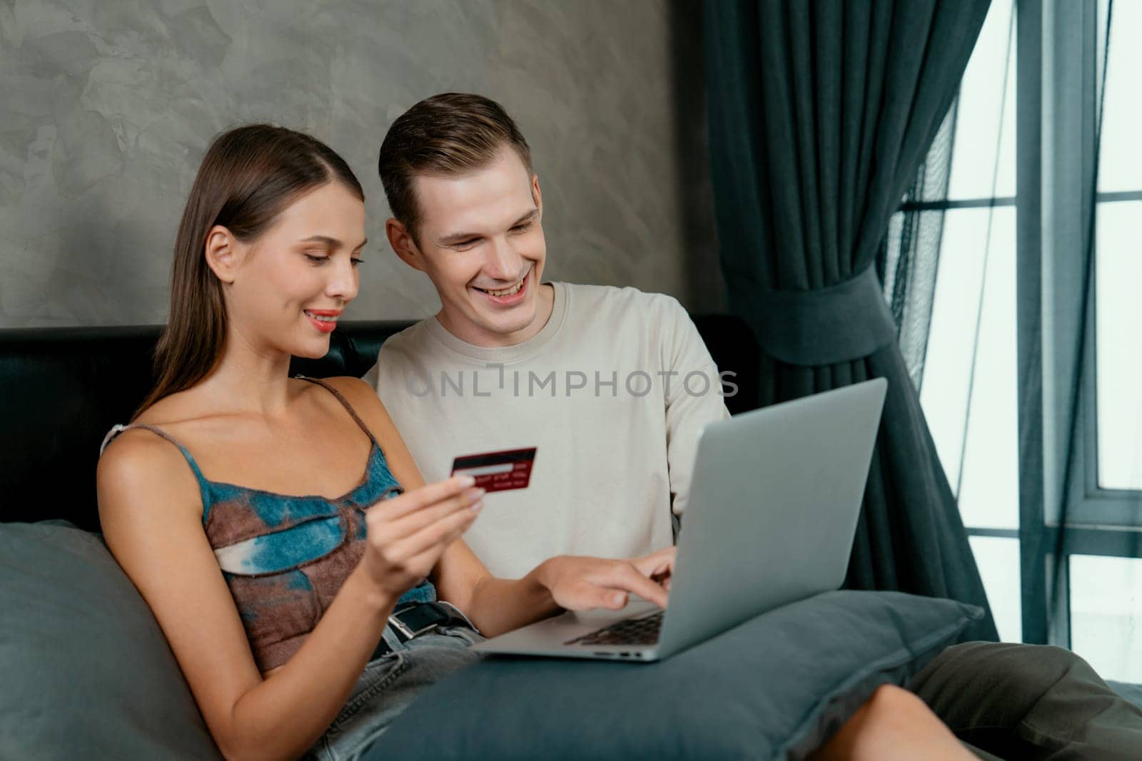 Young couple sit in the home bedroom using online payment app and digital wallet on smartphone to pay with credit card. E commerce shopping and modern purchasing via mobile internet. Unveiling