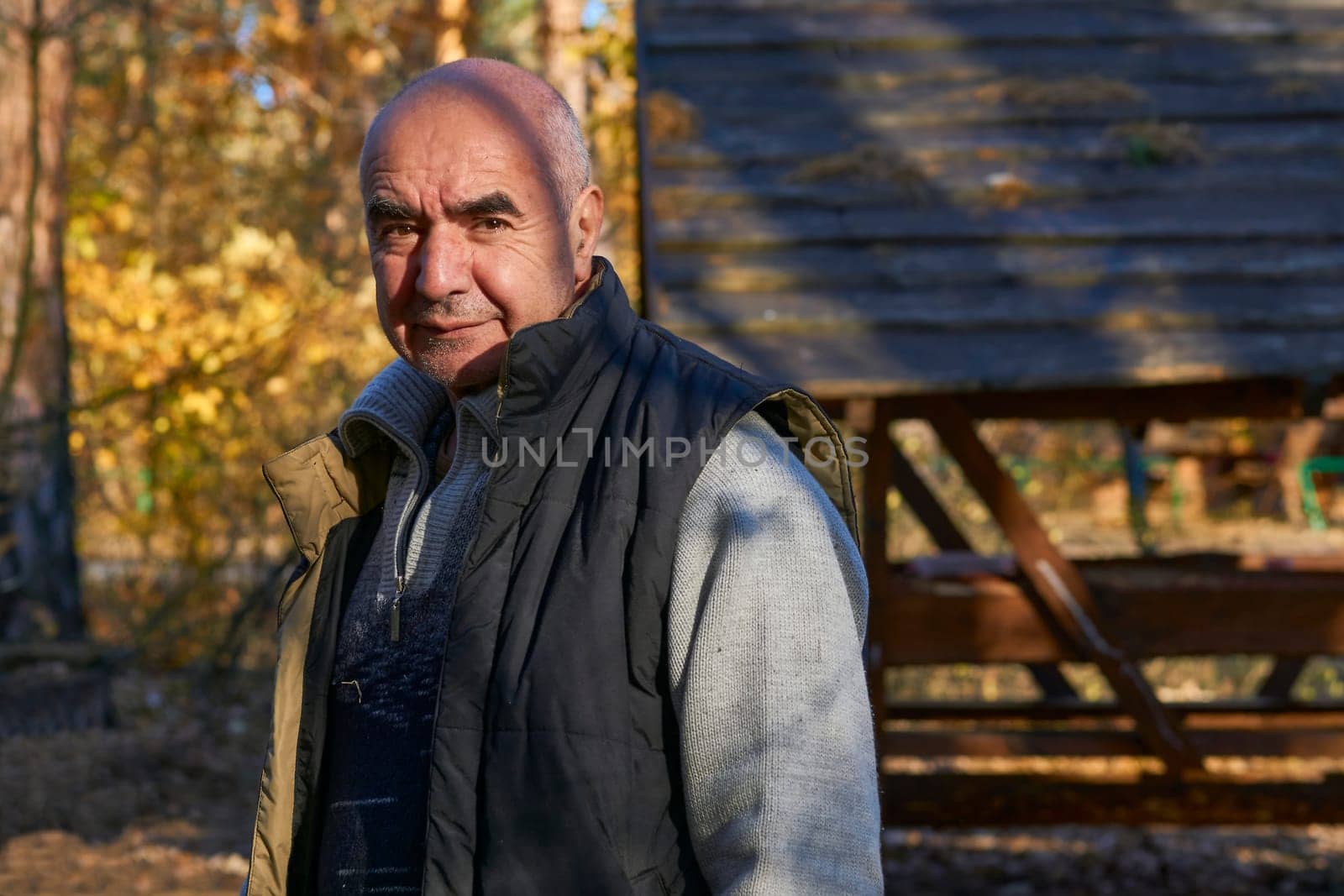 Cheerful elderly pensioner in a warm vest at a campsite on an autumn picnic by jovani68