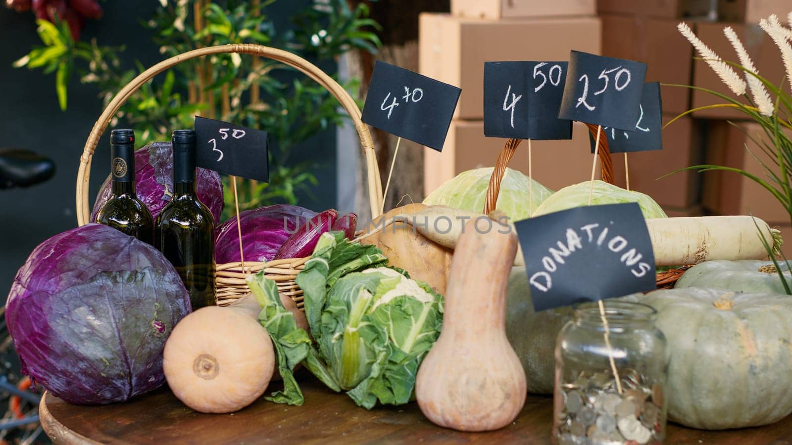 Variety of fresh locally grown lettuce and cabbage next to donations jar, colorful ripe natural products on farmers market stand. Organic produce on counter and table with coins. Close up.